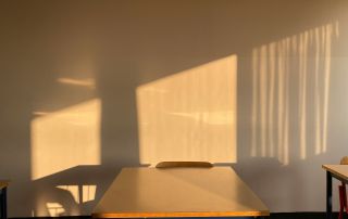 Ein einzelner Tisch steht in einem Klassenzimmer, die Sonne scheint darauf.